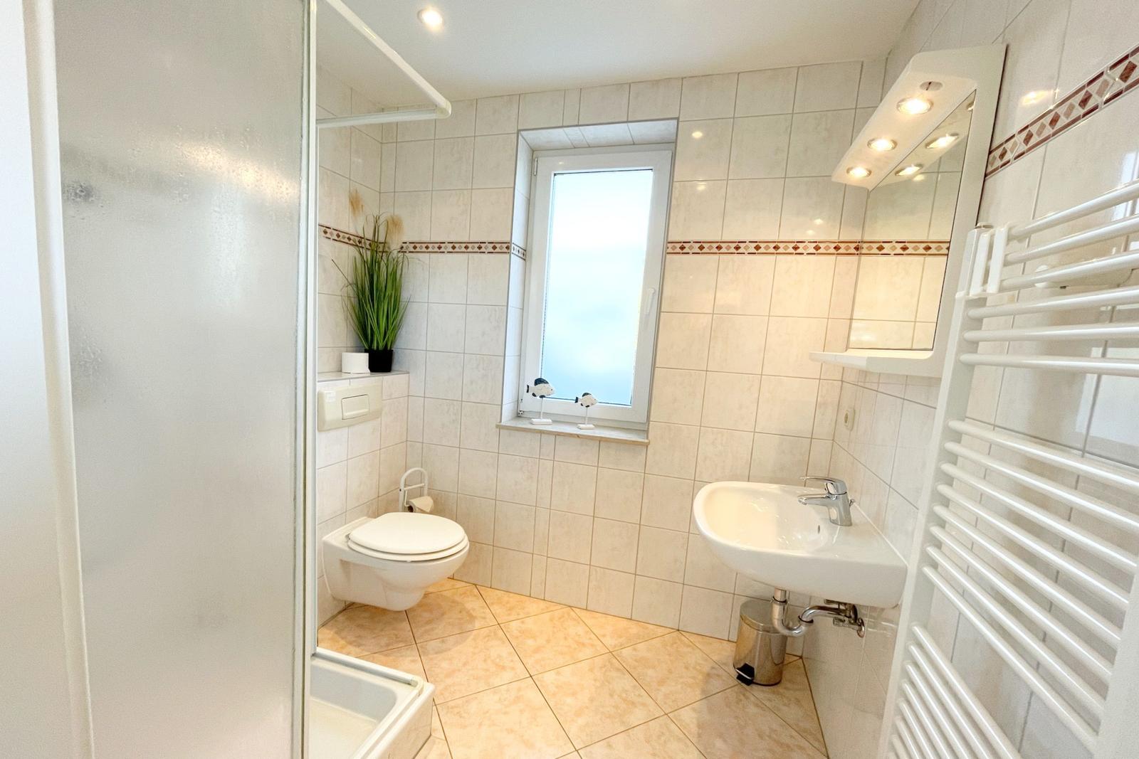 Badezimmer mit Toilette, Waschbecken und Fenster. Duschbereich mit Dusche.