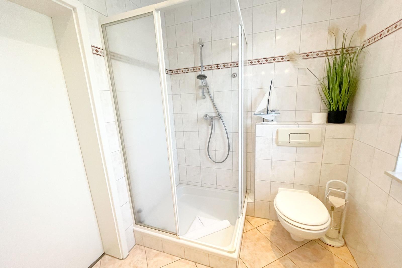 Bad mit Dusche, WC und Pflanze an der Wand.