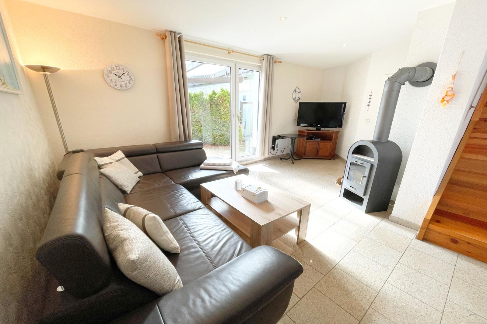 Wohnzimmer mit Ledersofa, Kaminofen und TV. Durchgang zur Terrasse.