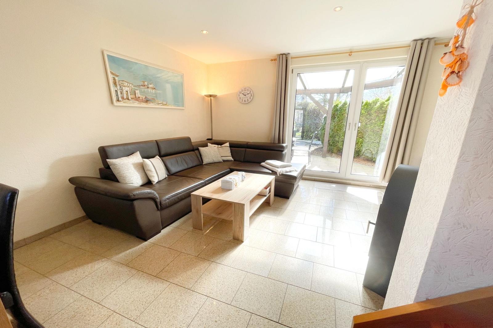 Wohnzimmer mit Ledersofa, Holztisch und Glastür zur Terrasse.