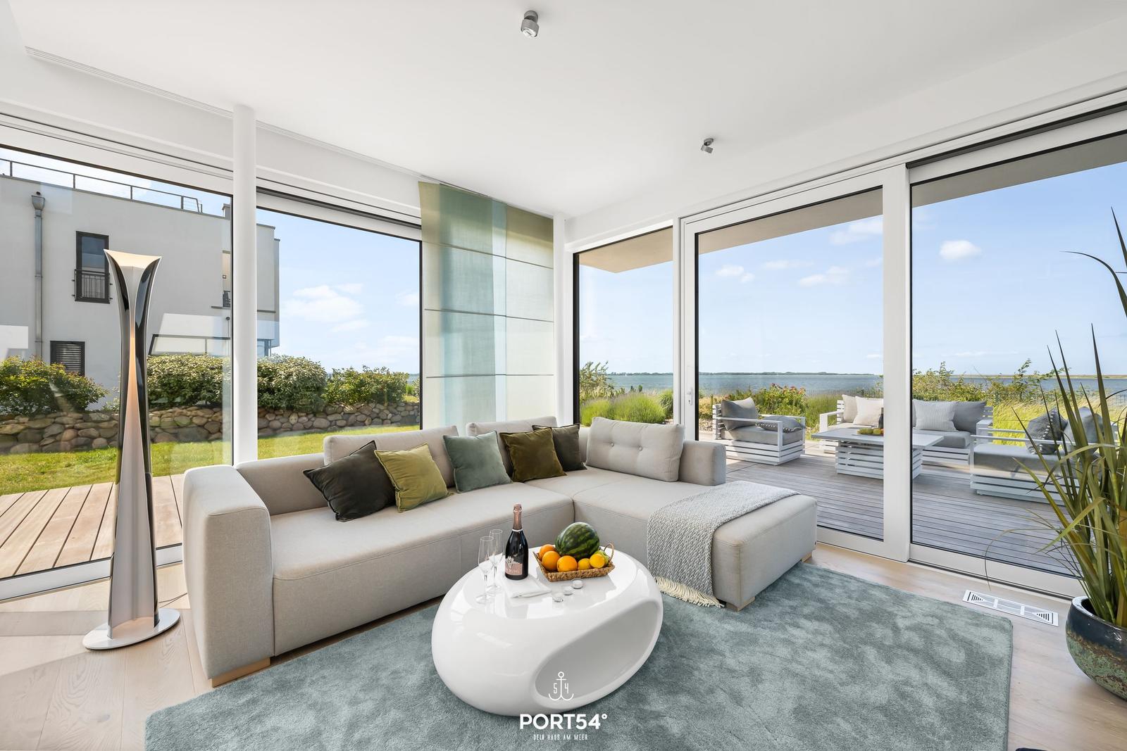 Wohnzimmer mit Sofa, Tisch und Aussicht auf Wasser und Terrasse.