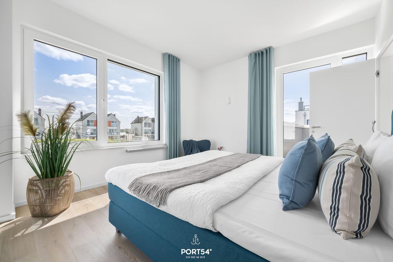Schlafzimmer mit Bett, Fenster und Pflanze. Blick auf Wohnhäuser.