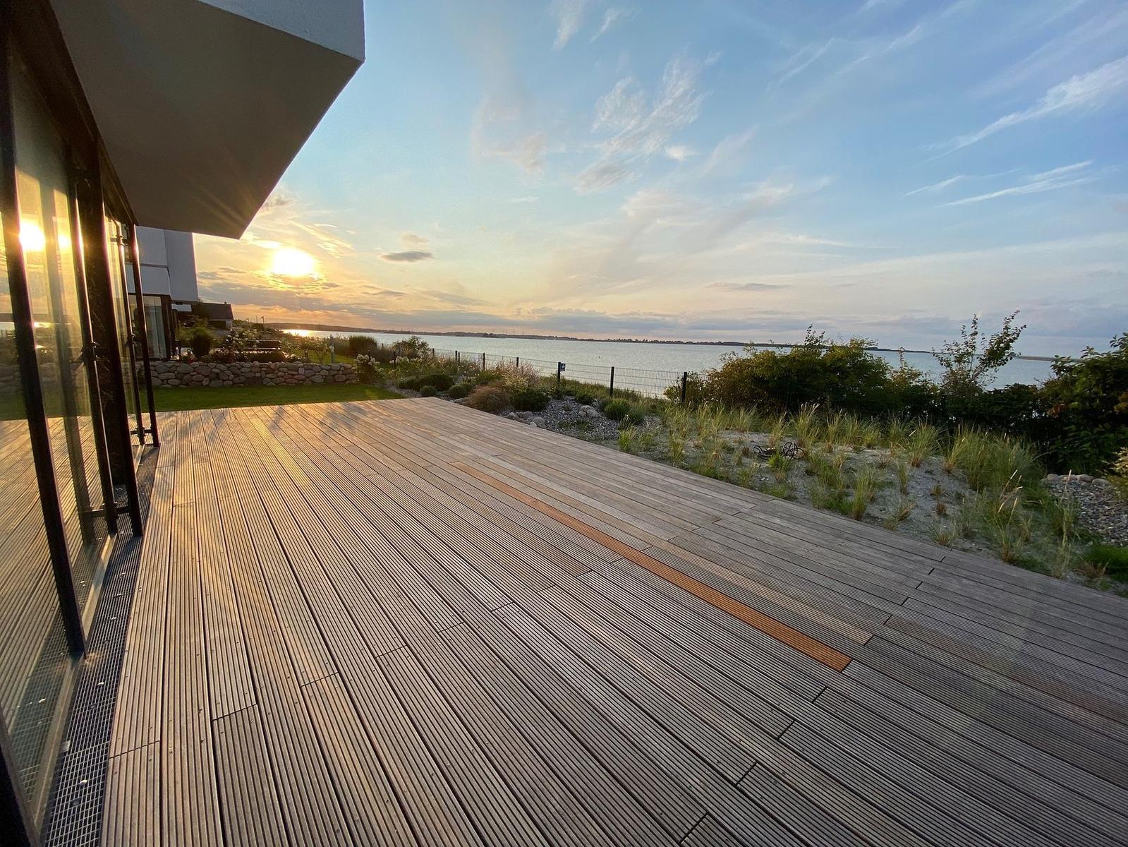 Terrasse mit Holzbelag blickt auf ruhiges Wasser bei Sonnenuntergang.