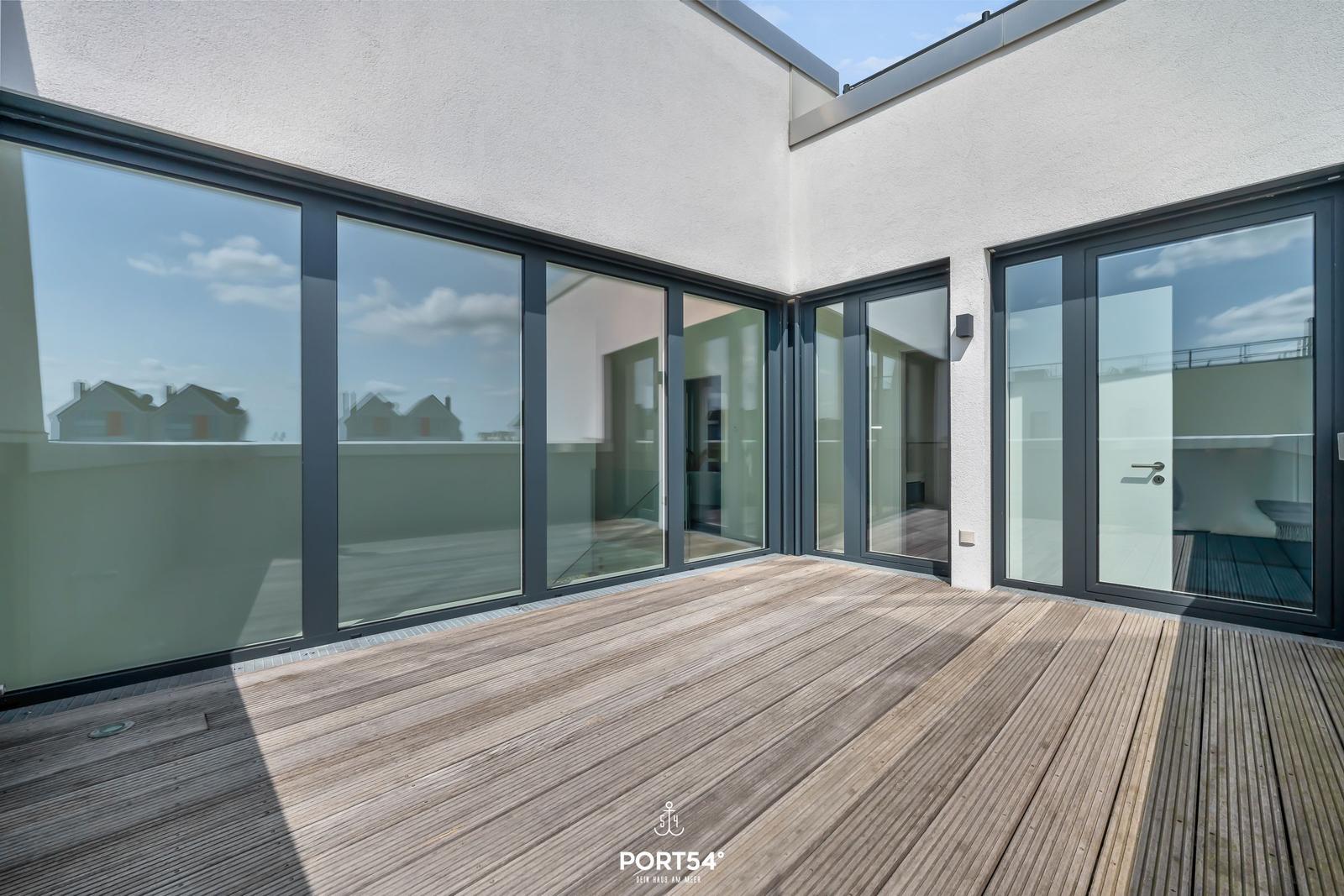 Terrasse mit Holzboden und großen Glasfenstern zur Wohnung.