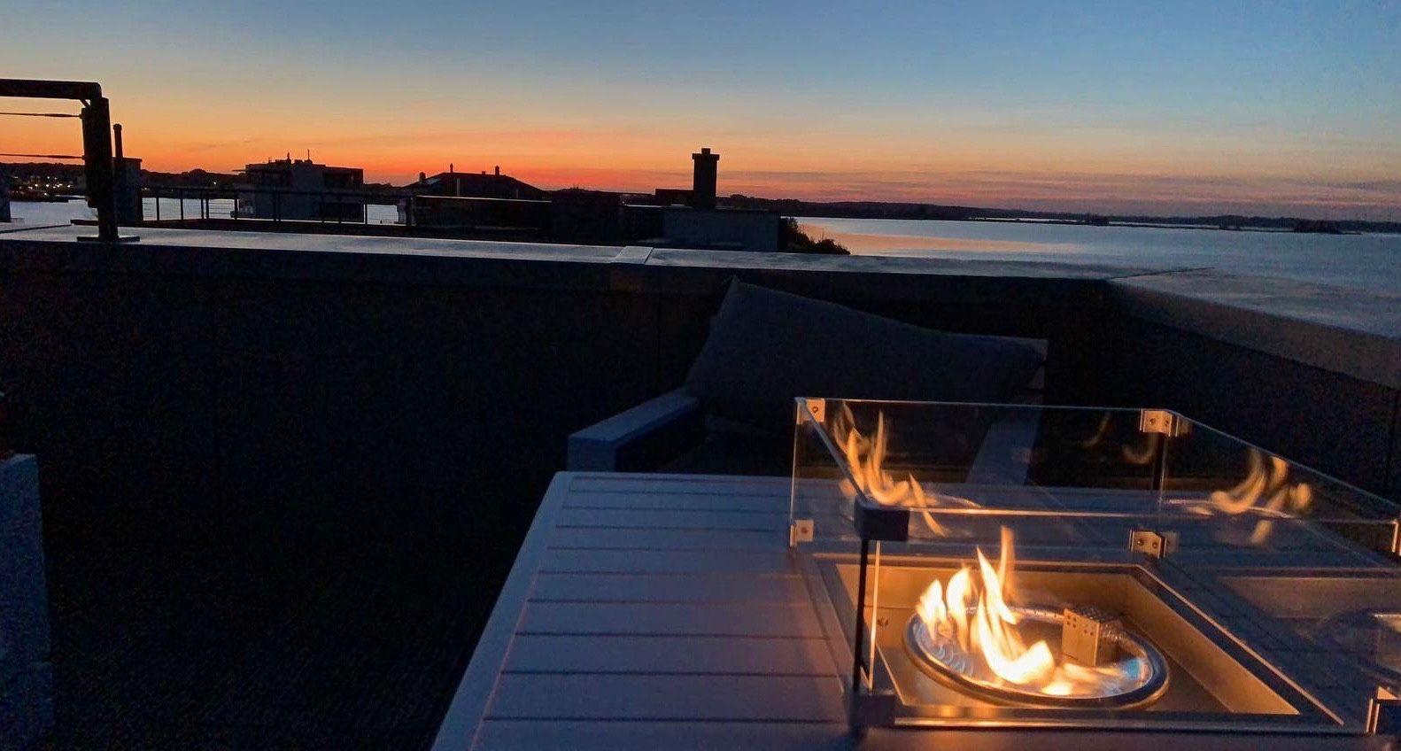 Rooftop mit Feuerkorb und Blick auf Wasser bei Sonnenuntergang.