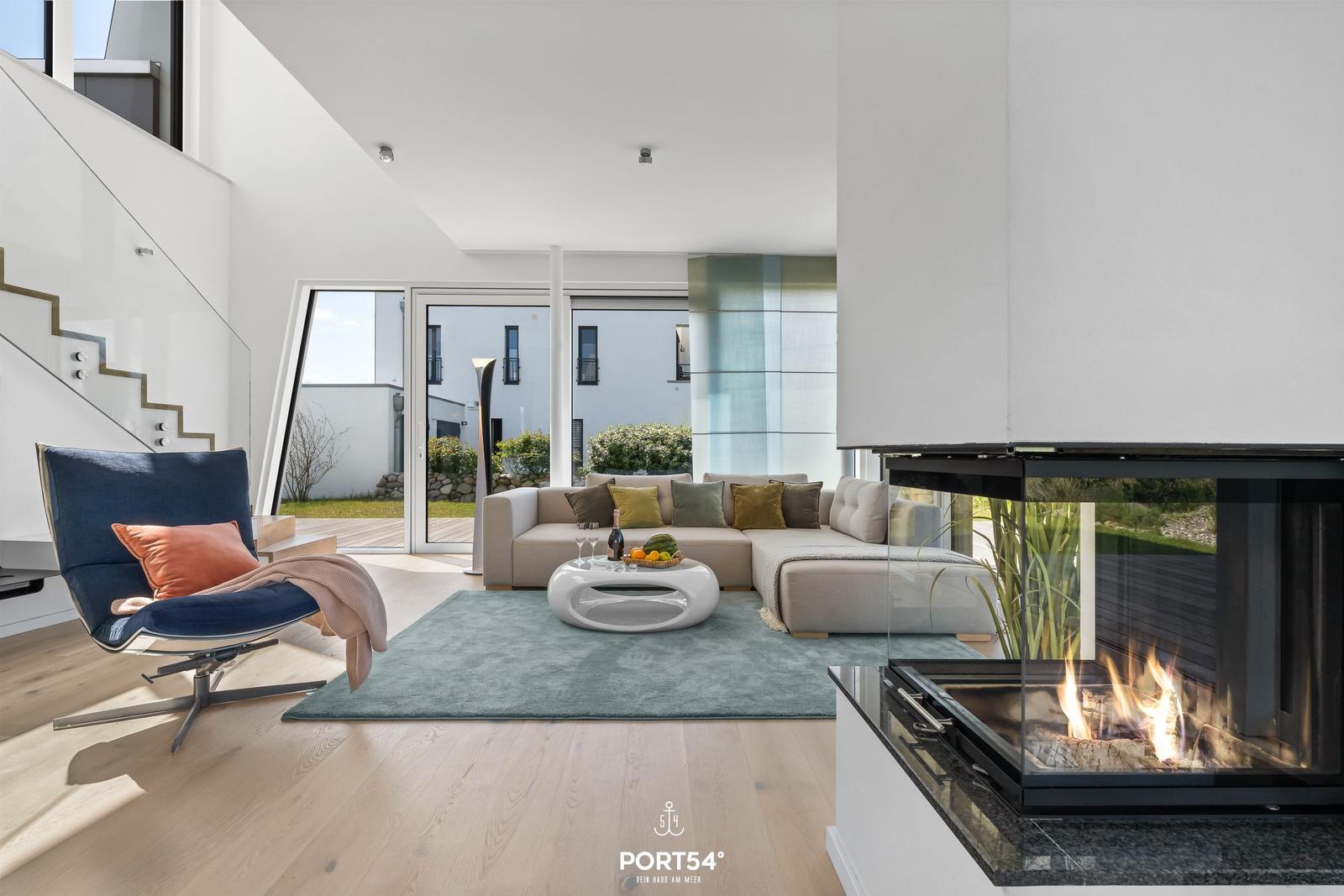 Modern eingerichteter Wohnbereich mit Kamin, Sofa und Stuhl. Durchgang zur Terrasse.