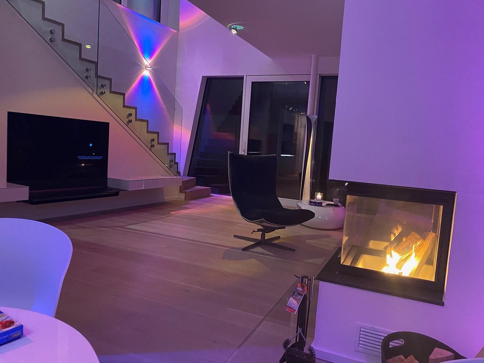 Wohnzimmer mit Kamin, Fernseher und moderner Treppe.