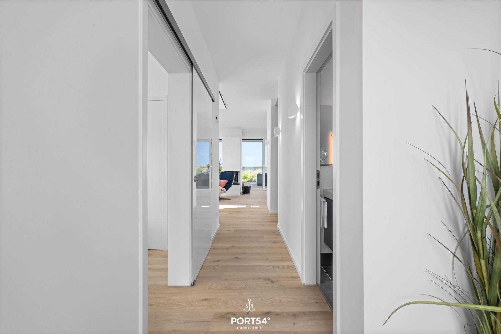 Flur mit Holzboden, weißen Wänden und Blick in Wohn- und Badezimmer.