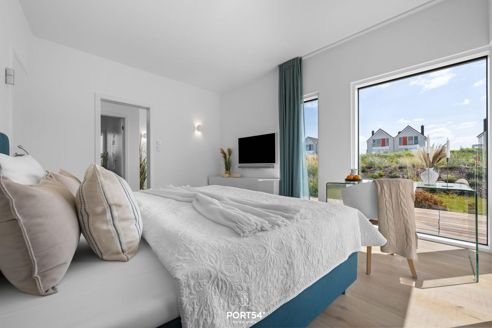 Schlafzimmer mit Bett, Fernseher und großem Fenster mit Blick auf die Außenanlage.