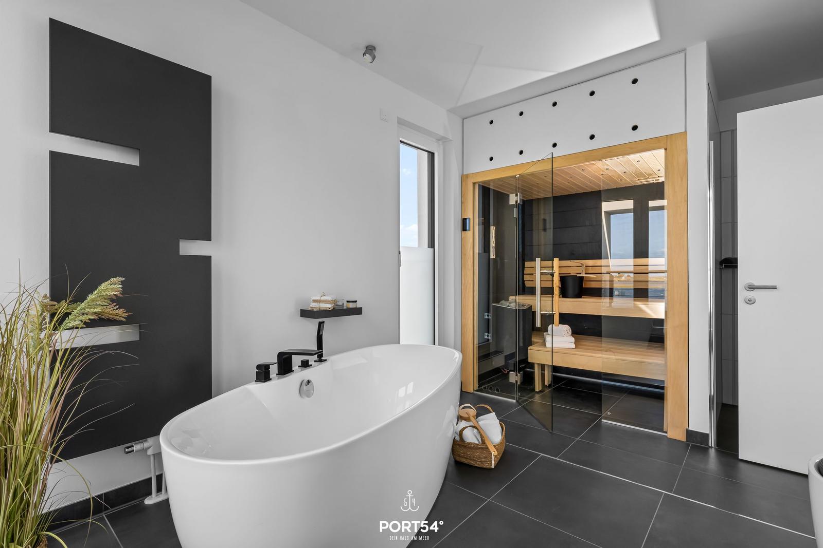 Bad mit freistehender Badewanne und Sauna mit Glaswand.