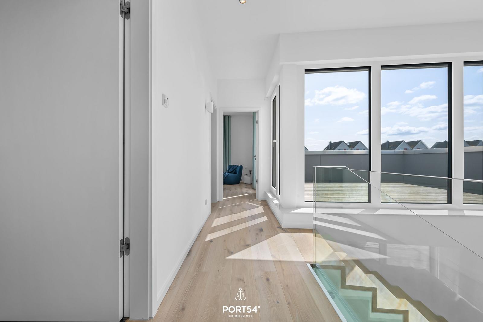 Flur mit Holzboden, Glasgeländer und Blick auf Balkon.
