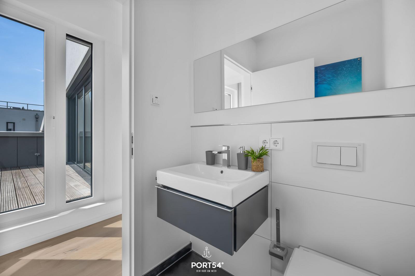 Badezimmer mit Waschbecken, Spiegel und Blick auf Balkon.