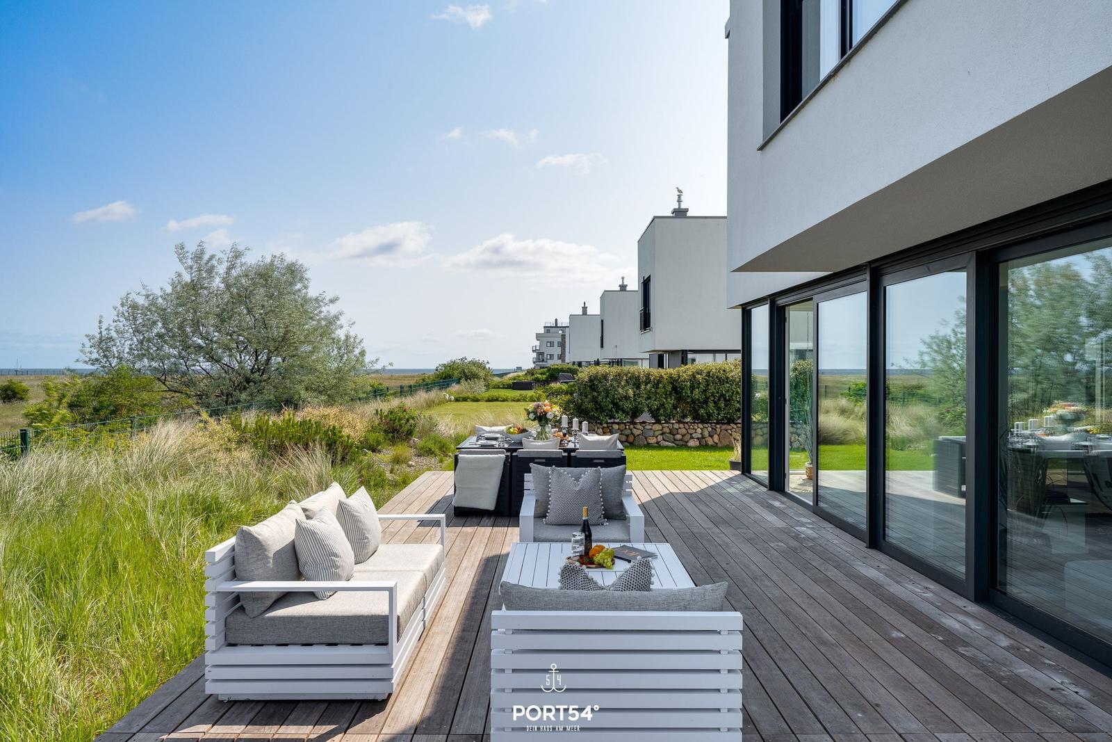 Terrasse mit Sitzgruppe und Tisch. Blick auf Grünfläche und moderne Häuser.