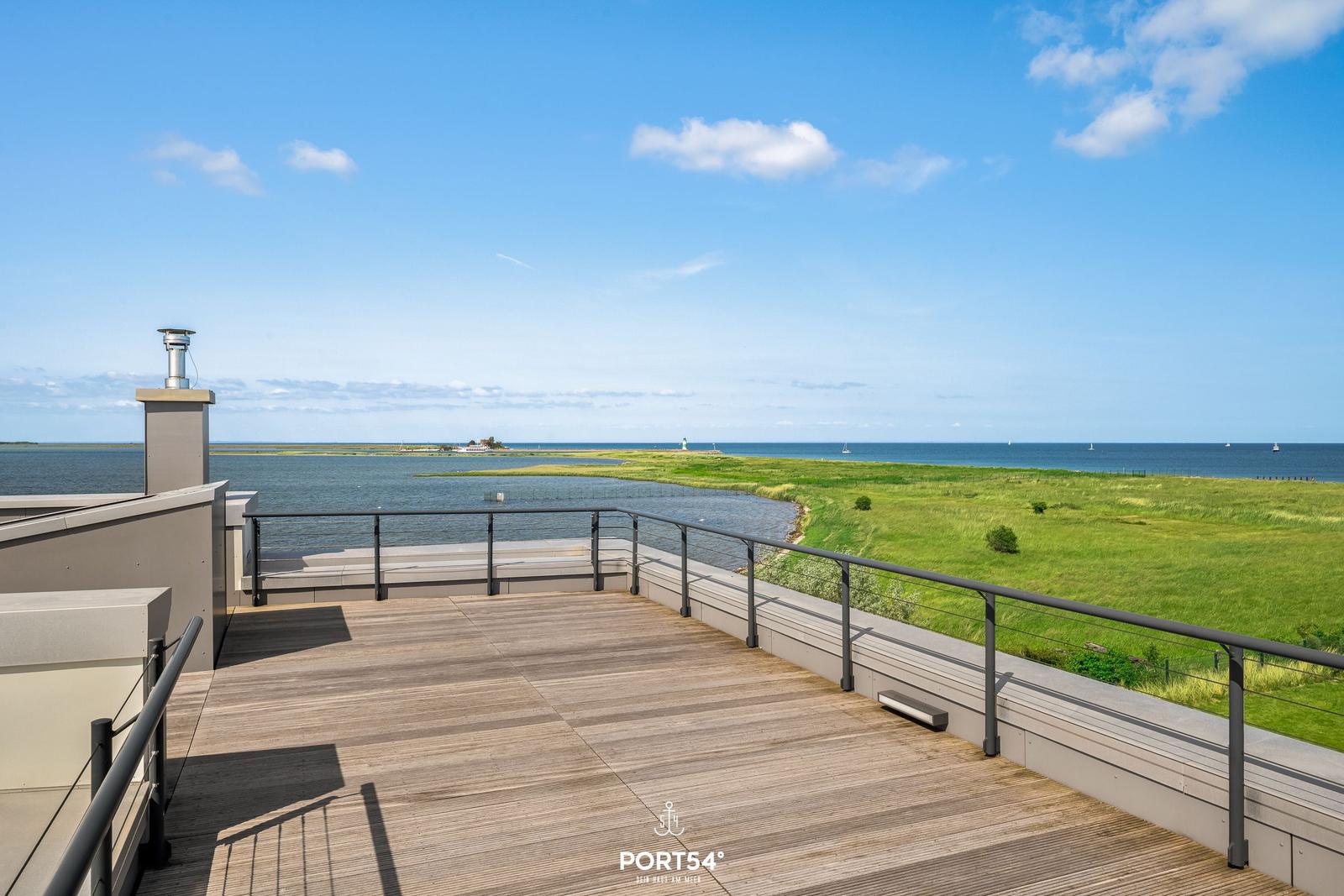 Terrasse mit Blick auf Wasser und Grünland unter blauem Himmel.