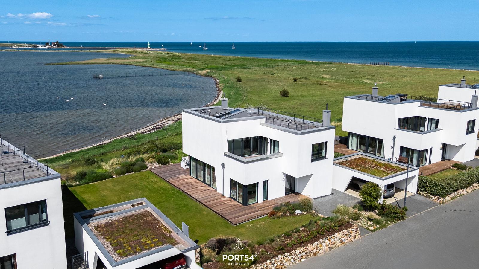 Moderne weiße Häuser am Wasser mit Terrassen und Grünflächen.