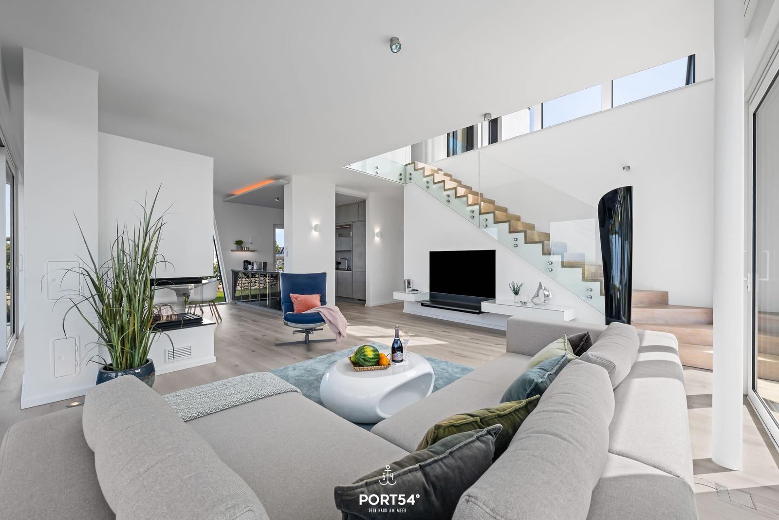 Wohnbereich mit Sofa, Fernseher und Treppe zur oberen Etage.