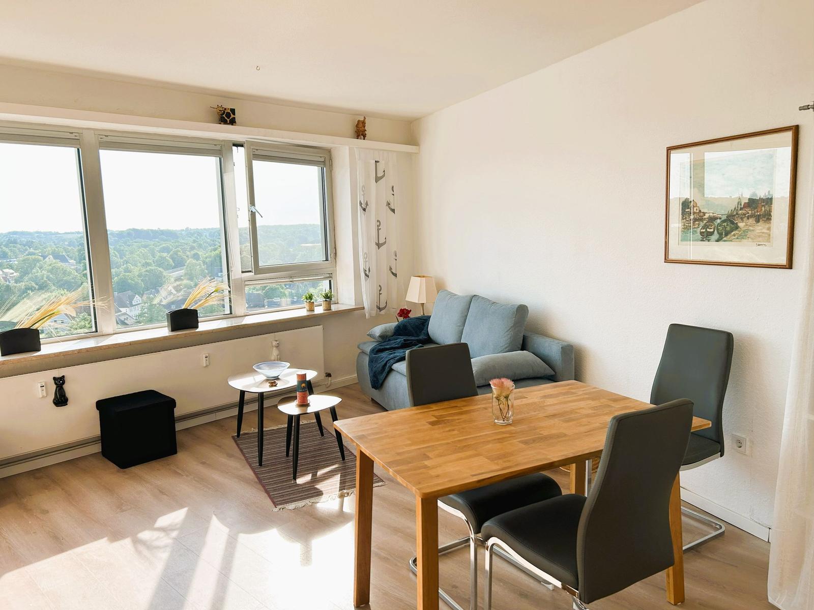 Wohn- und Essbereich mit Blick auf grüne Landschaft. Holztisch, Sofa und Fenster.