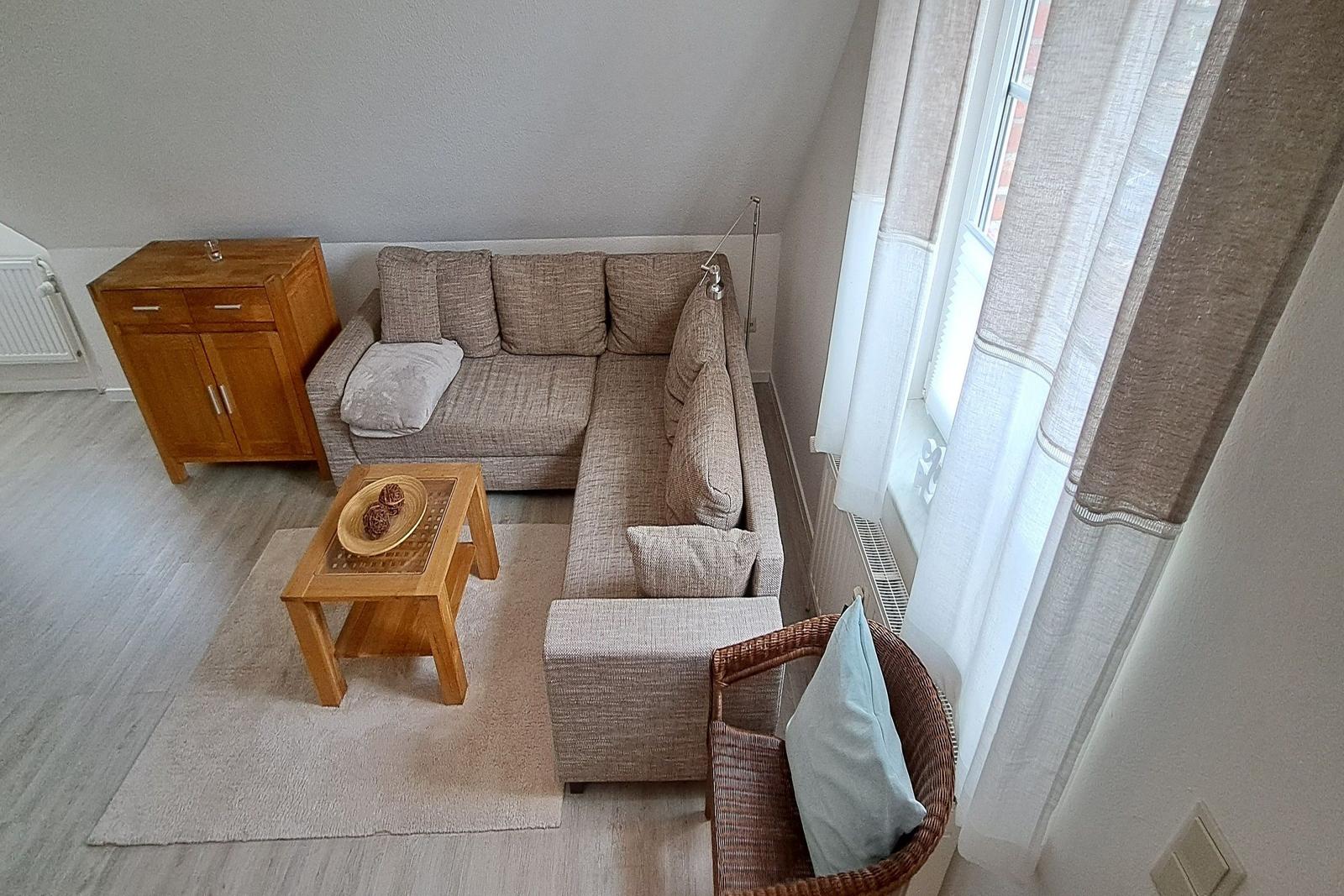 Wohnzimmer mit Ecksofa, Holztisch und Fenster mit Vorhängen.