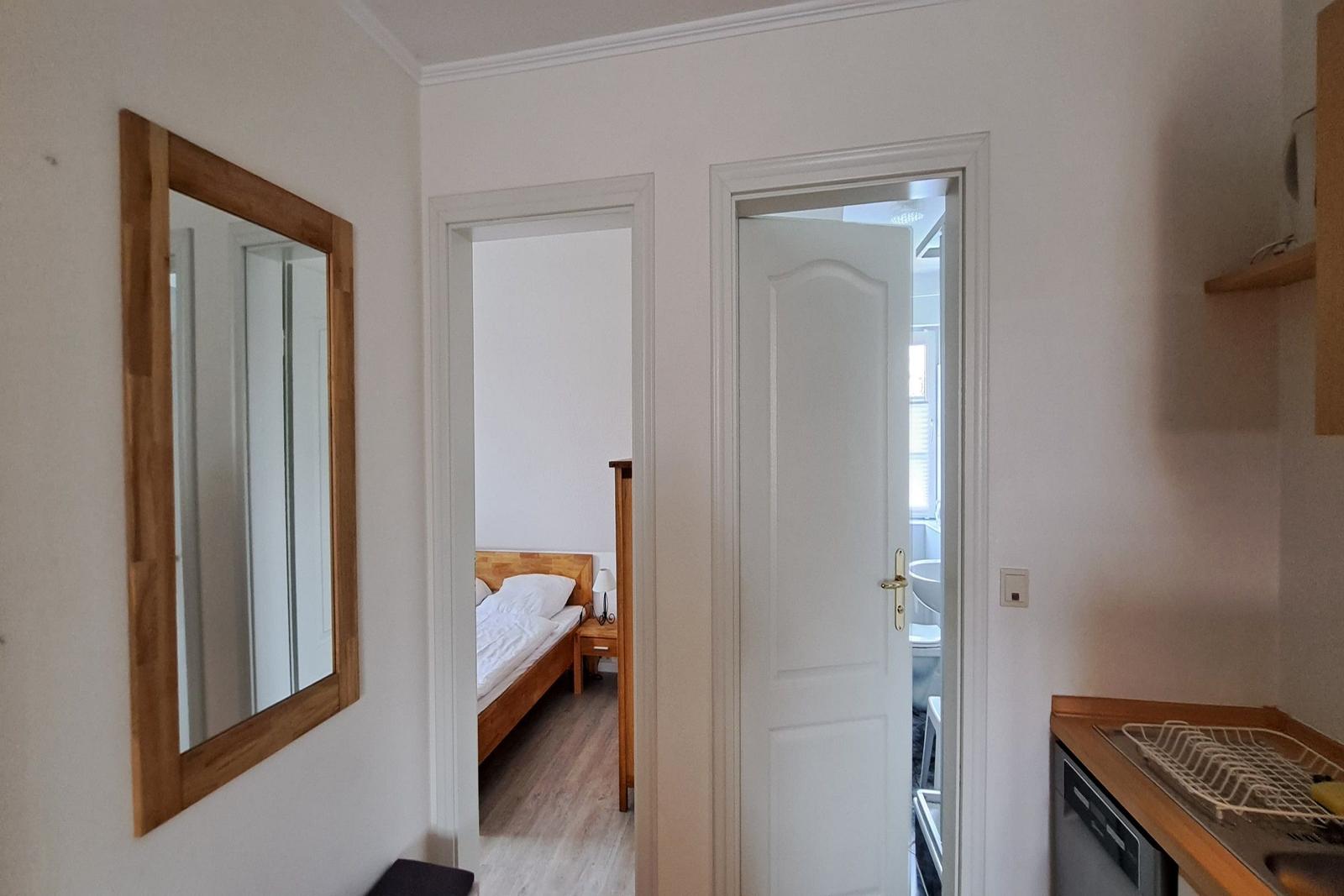 Halle mit Spiegel, Schlafzimmer und Bad. Küchenbereich mit Spüle und Geschirr.