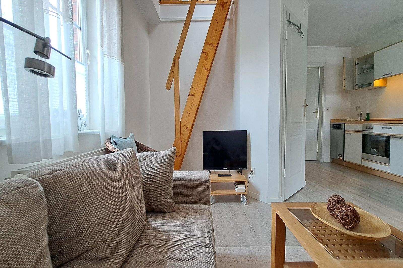 Wohnzimmer mit Sofa, TV und Holztreppe. Küche im Hintergrund.