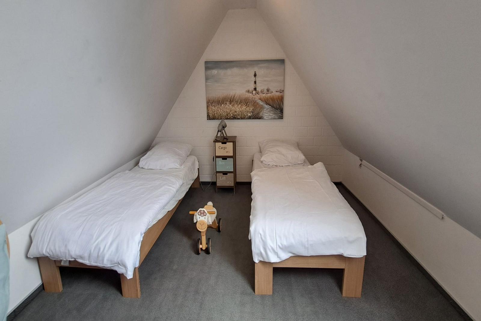 Zwei Einzelbetten in einem Dachzimmer mit Wandbild und Kinderwagen.