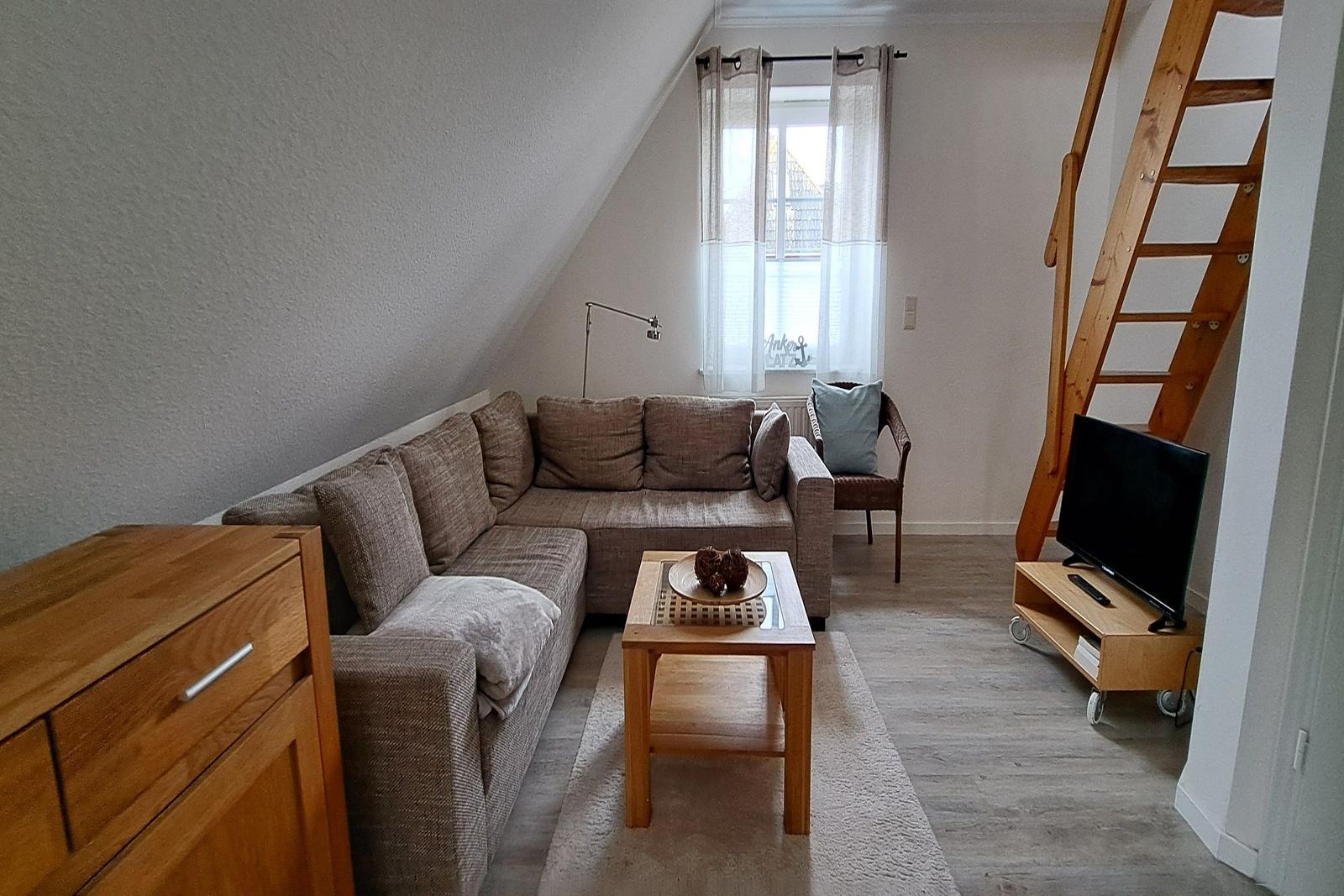 Wohnzimmer mit Sofa, TV und Holztreppe.
