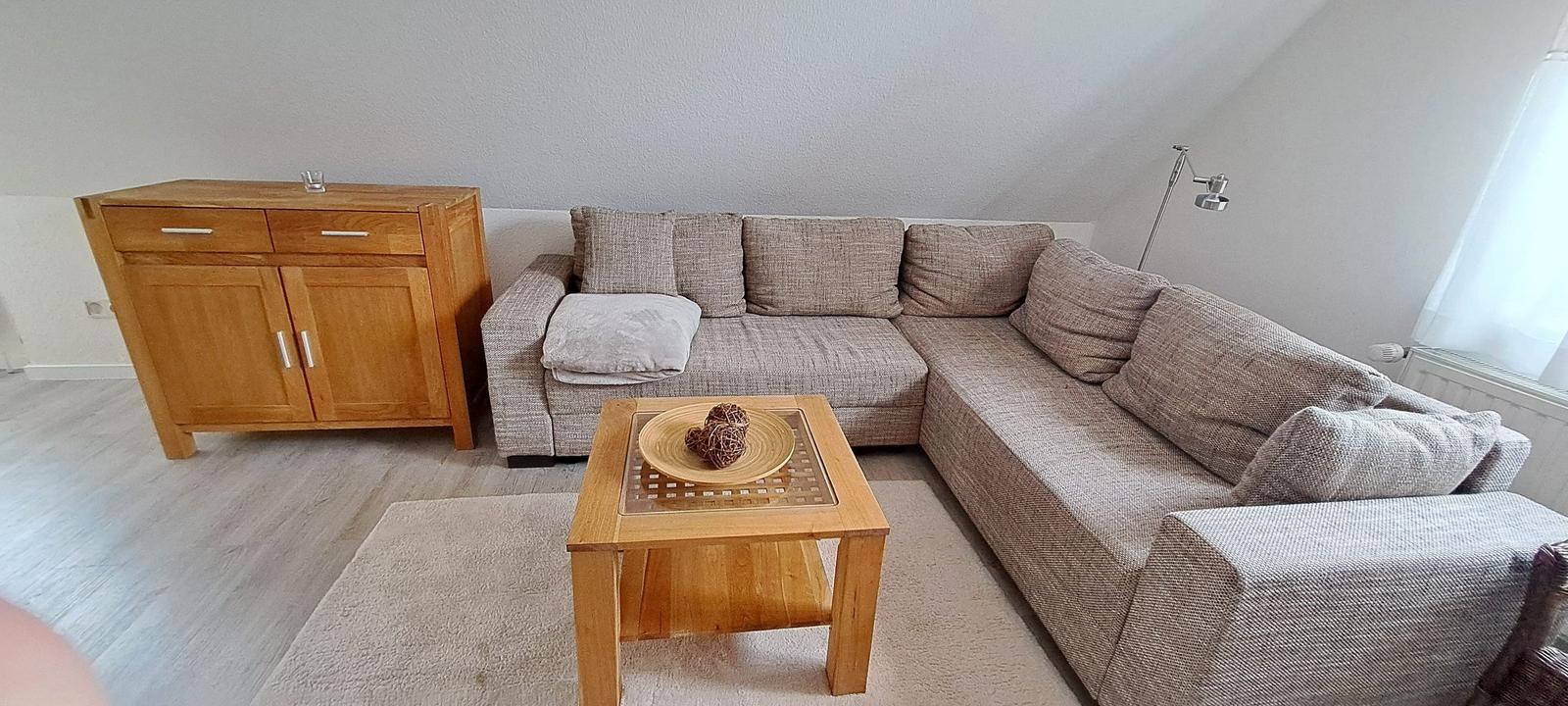 Wohnzimmer mit Ecksofa, Holztisch und Sideboard.