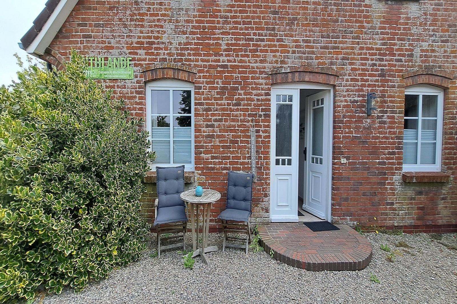 Rotes Backsteinhaus mit weißer Tür und Sitzgruppe vor dem Eingang.