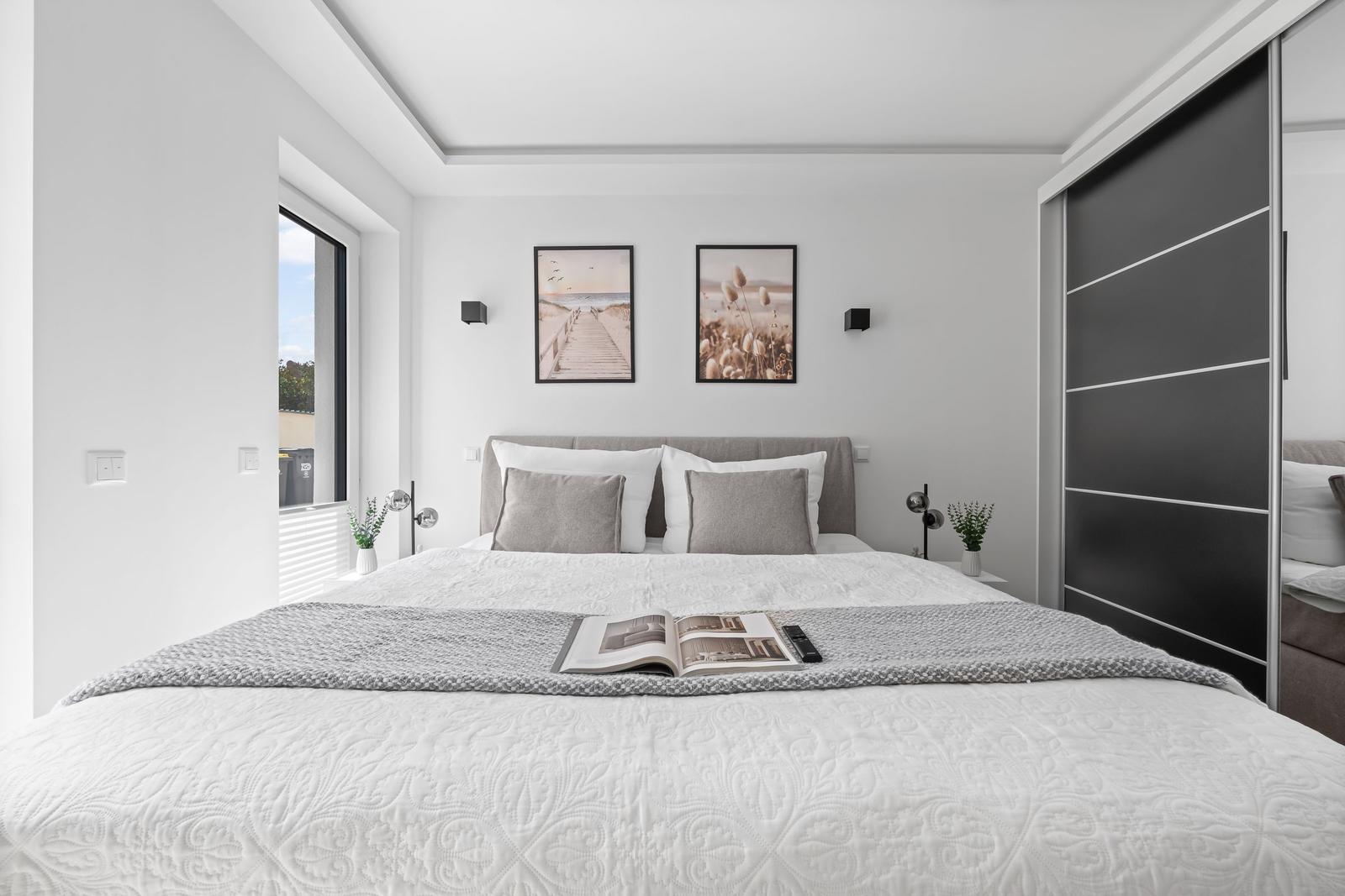 Schlafzimmer mit Bett, Wandbildern und Schwebetüren.