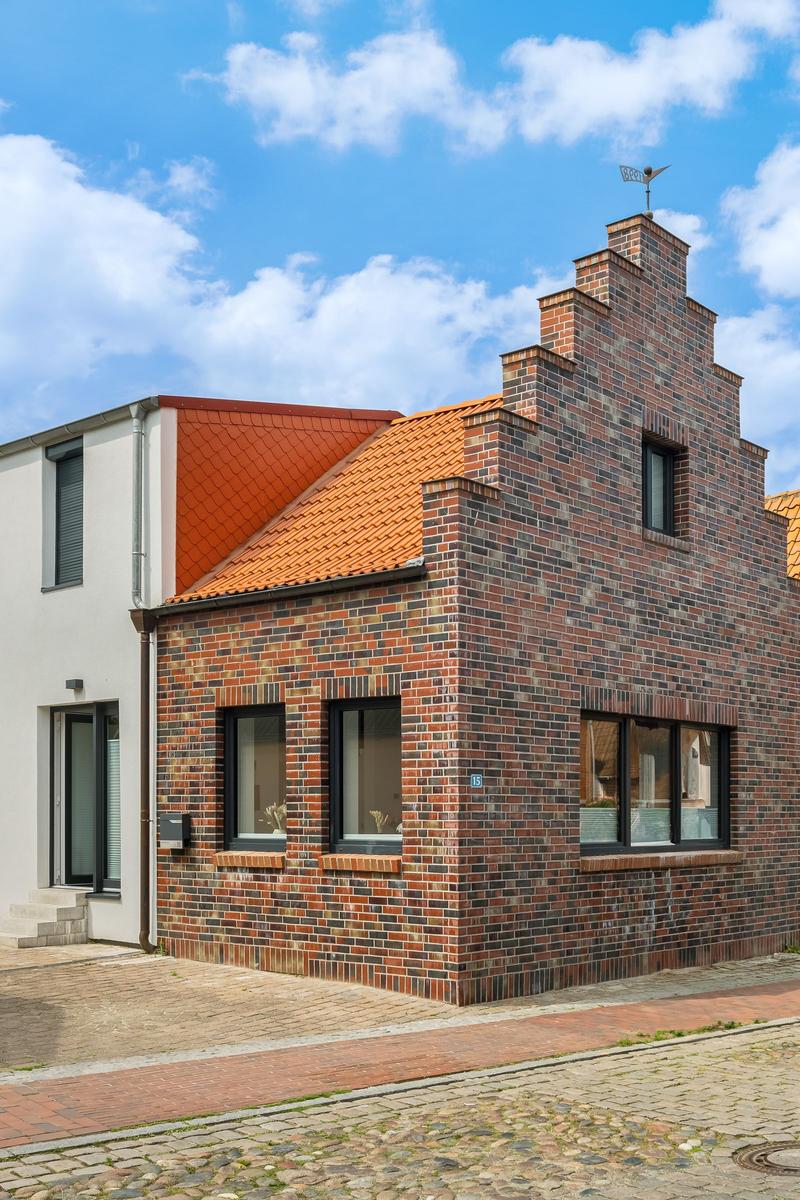 Haus mit Backsteinfassade und rotem Dach unter blauem Himmel.