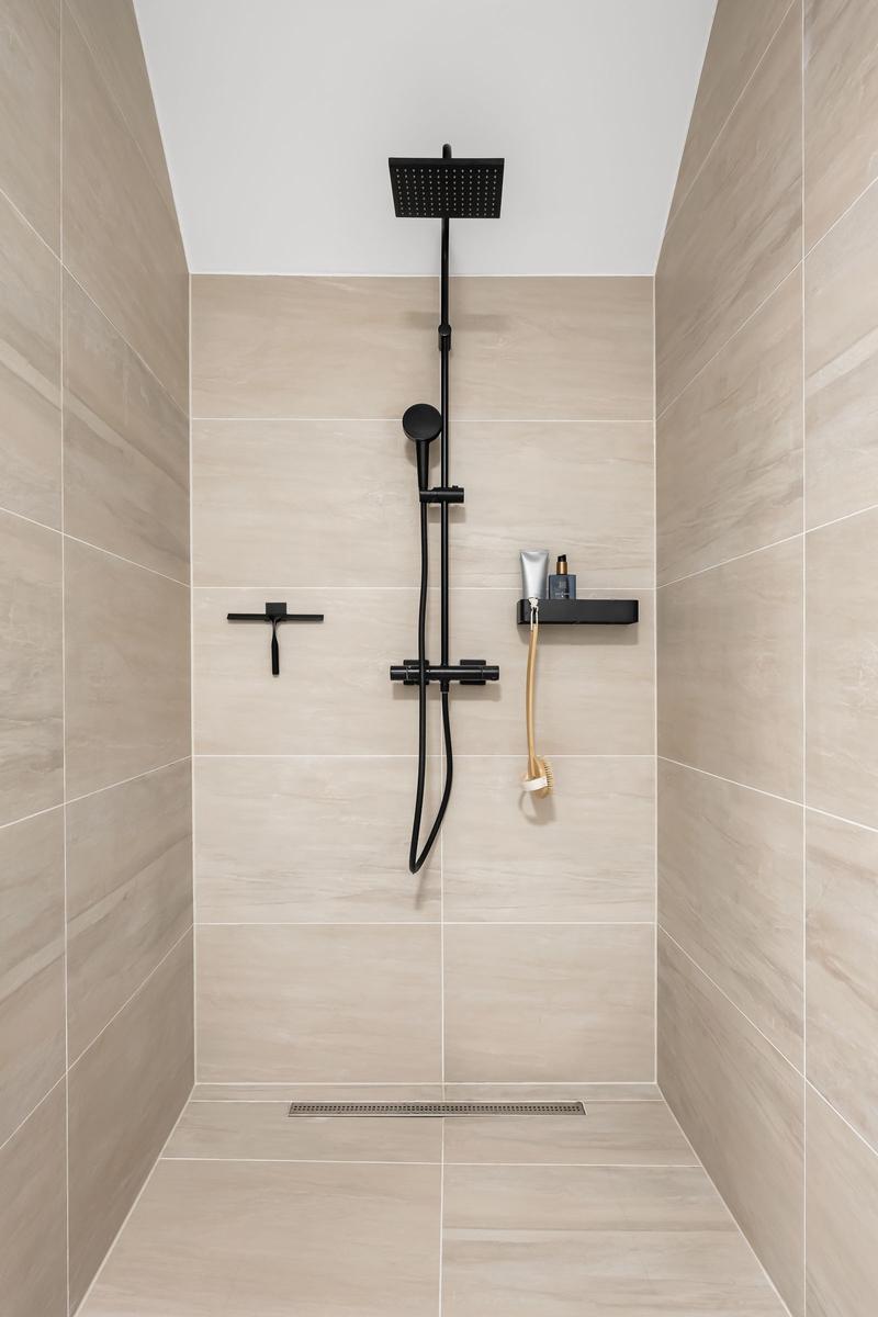 Duschkabine mit schwarzer Dusche und hellen Fliesen.