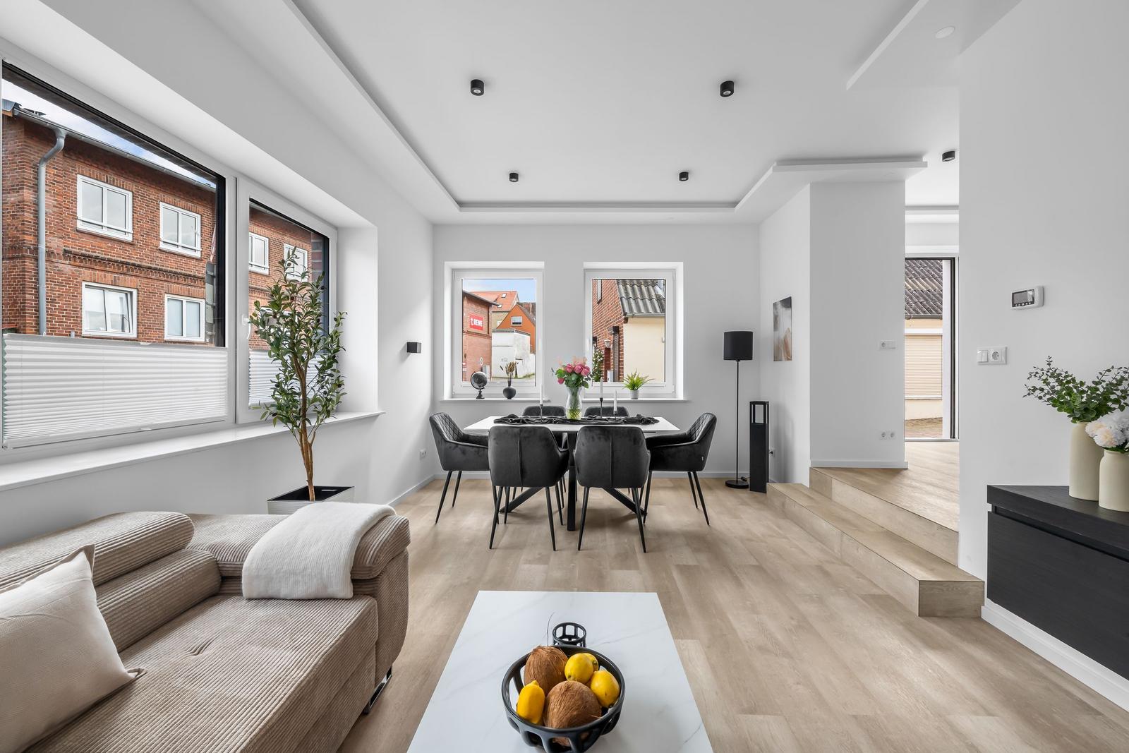 Wohn- und Essbereich mit Holzboden, Sofa, Esstisch und Blick auf Gebäude.