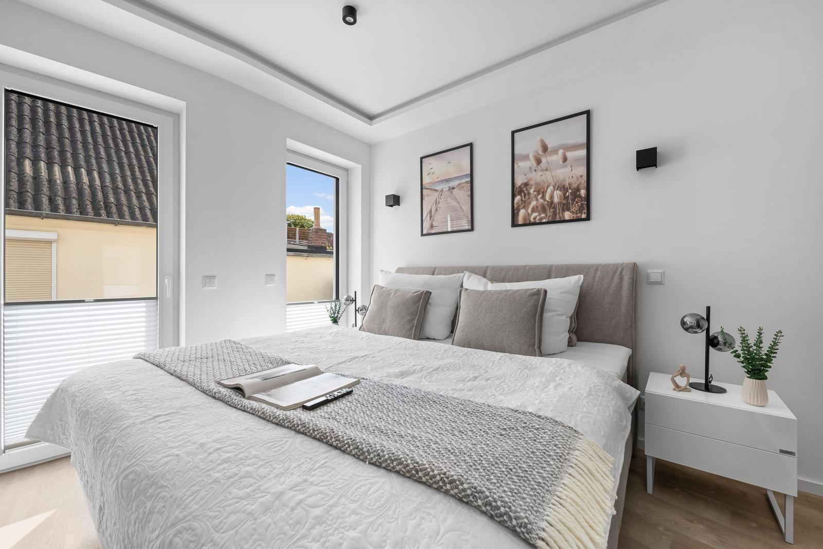 Schlafzimmer mit Bett, Nachttisch und Fenstern.