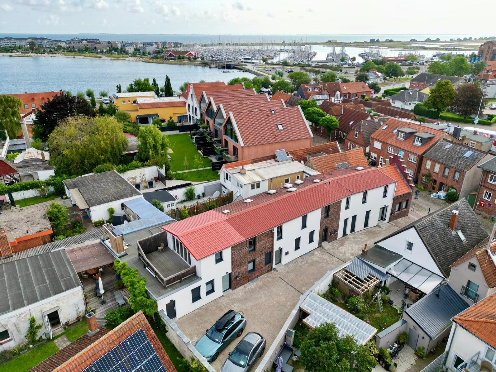 Häuser mit roten Dächern am Wasser, Marina im Hintergrund.