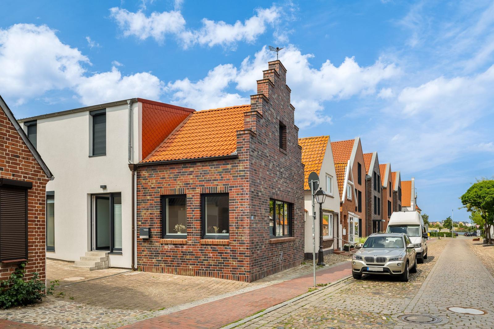 Reihenhaus mit rotem Dach und Backsteinfassade an einer Straße mit Kopfsteinpflaster.