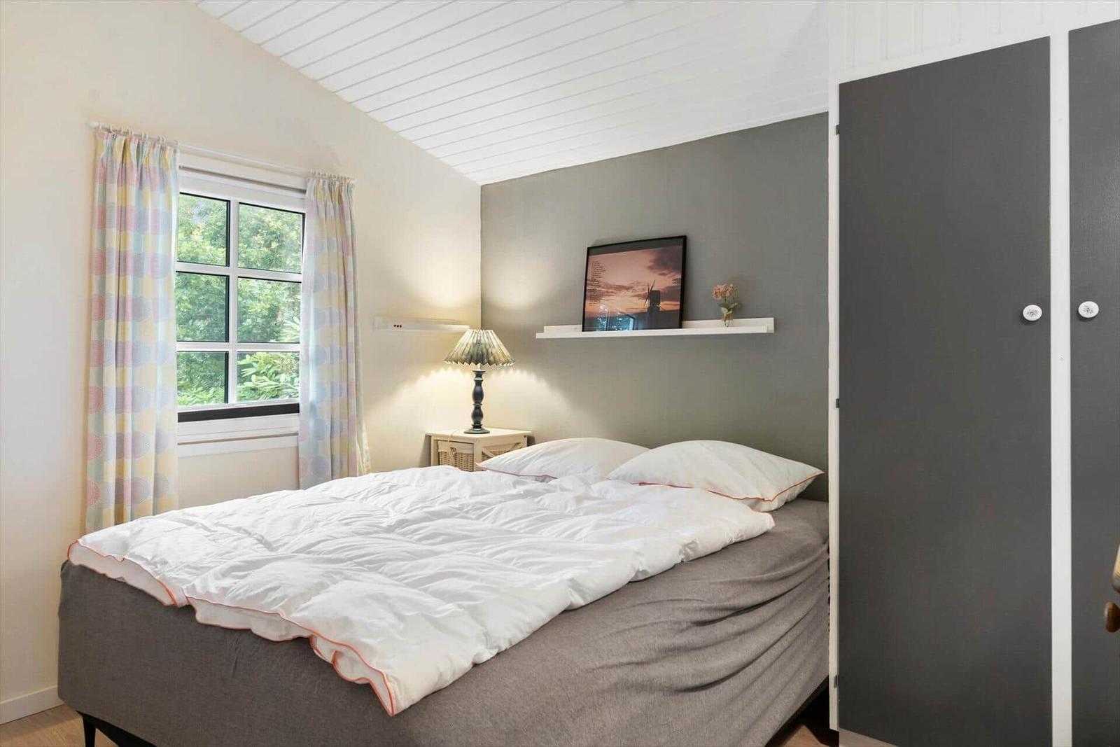 Schlafzimmer mit Bett, Fenster und Kleiderschrank. Wandbild und Nachttisch sichtbar.