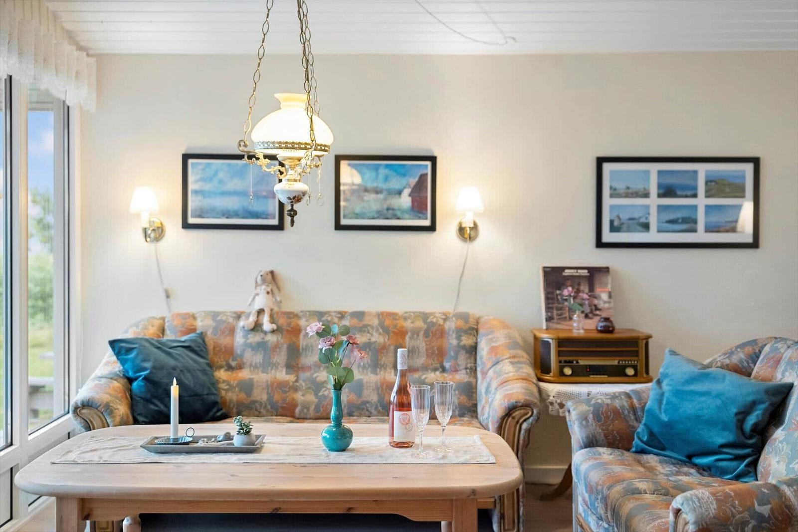Wohnzimmer mit Sofa, Couchtisch und Wandbildern. Ein Kronleuchter hängt über dem Tisch.