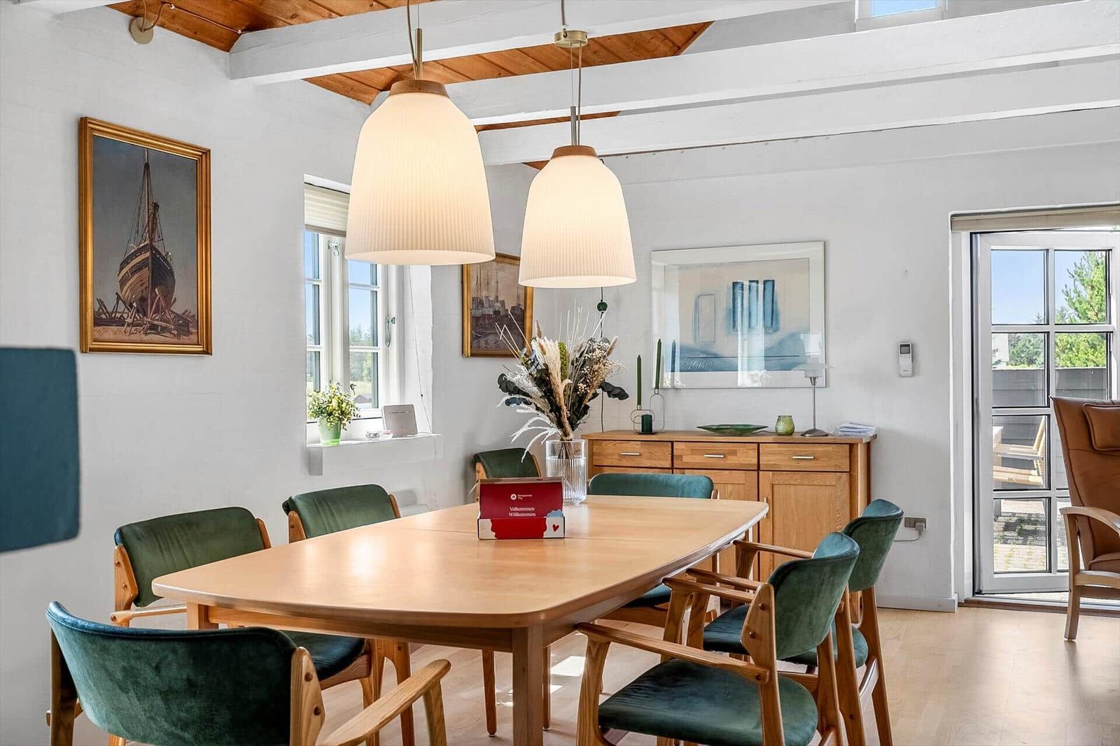Esszimmer mit Holztisch, grünen Stühlen und zwei hängenden Lampen.