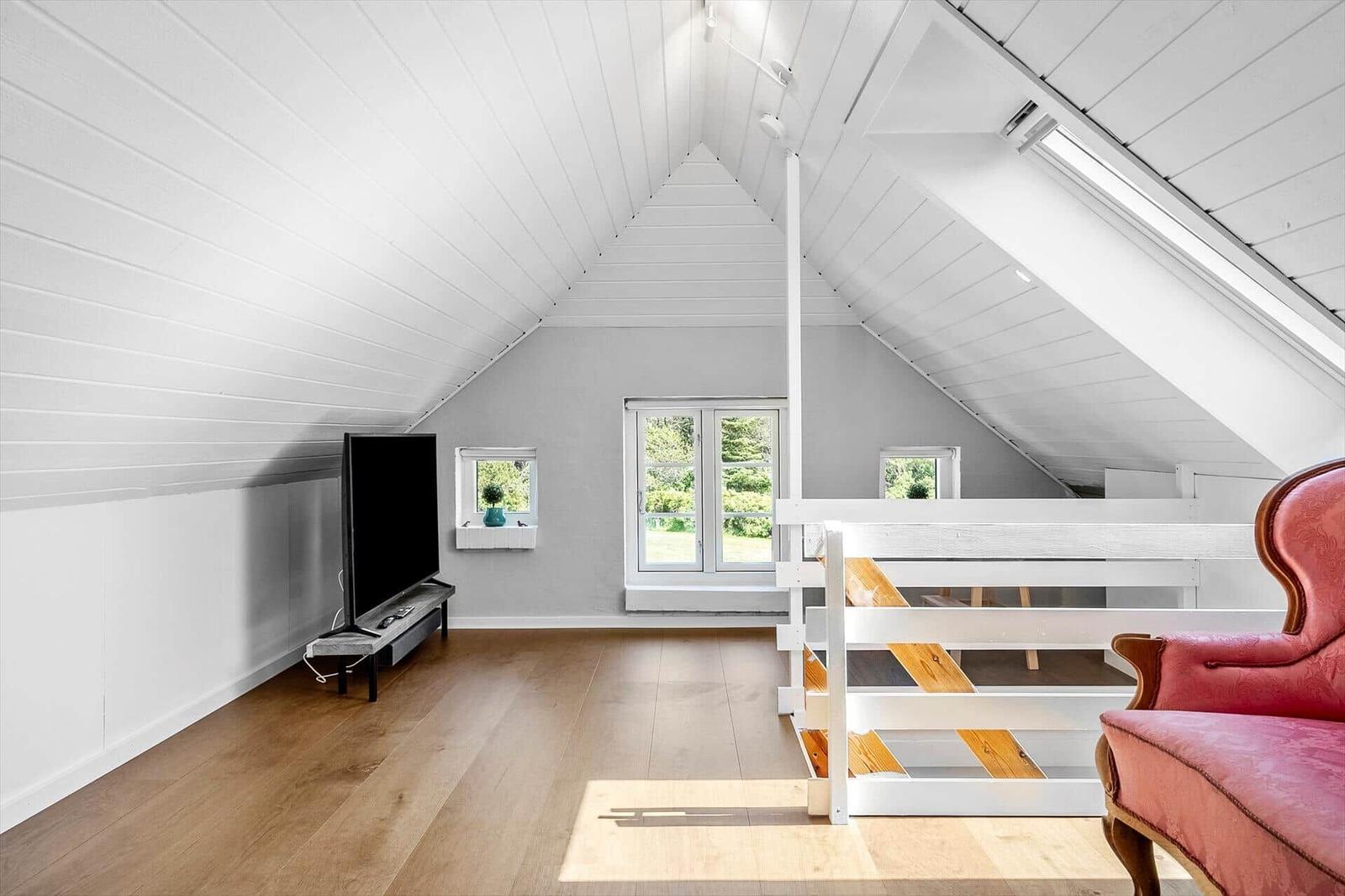 Dachgeschosszimmer mit Fernseher, rotem Sessel und Fenster zur Außenseite.
