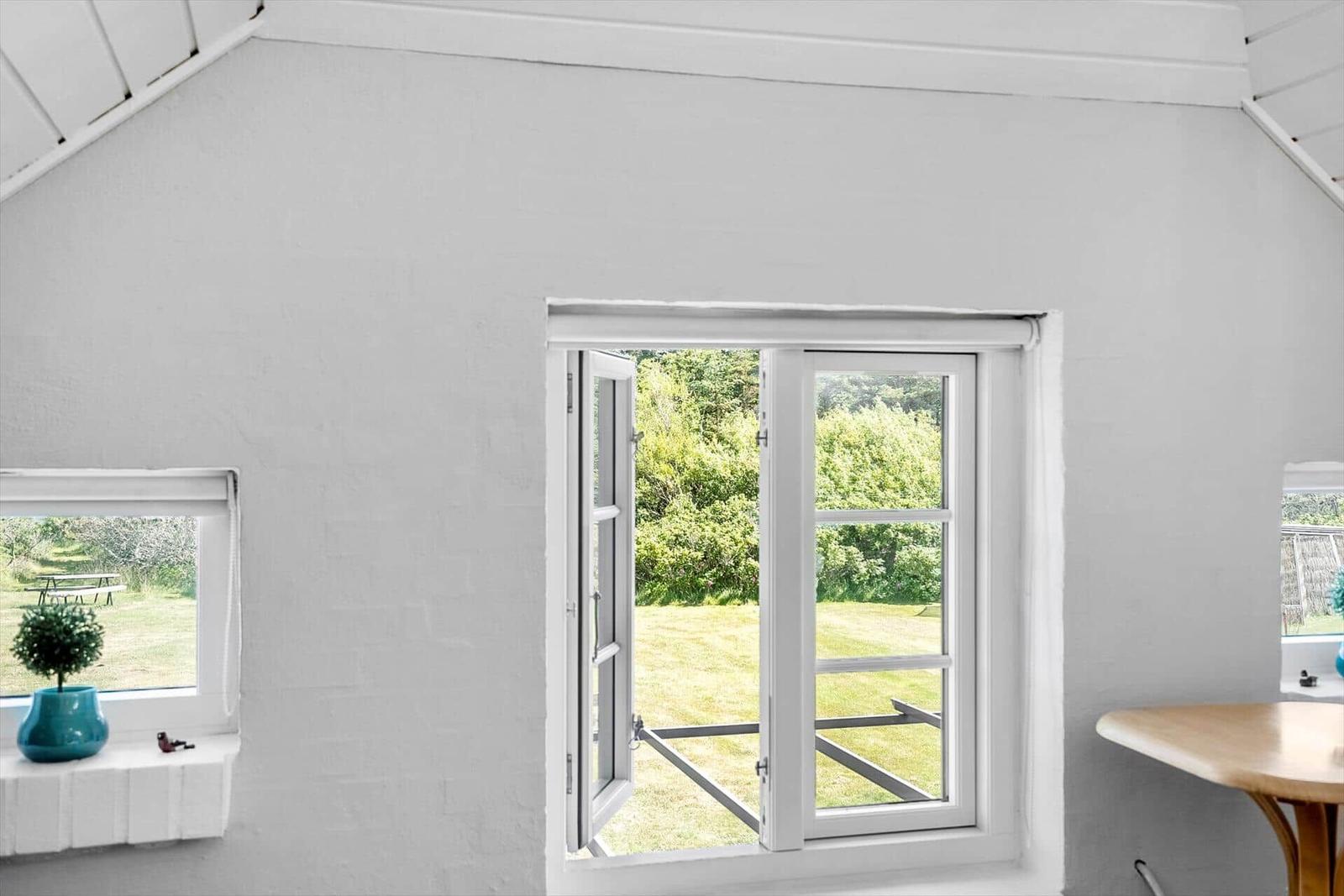 Ein Raum mit weiß gestrichenen Wänden und einem offenen Fenster zum Garten.