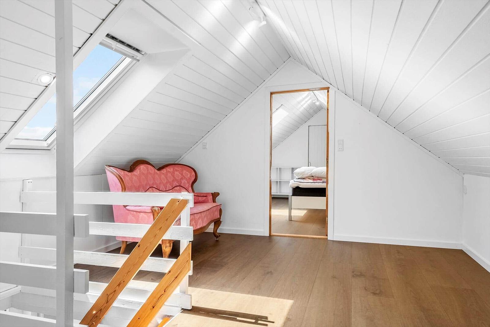 Schlafzimmer mit Dachschrägen, Holzboden und rosa Sofa