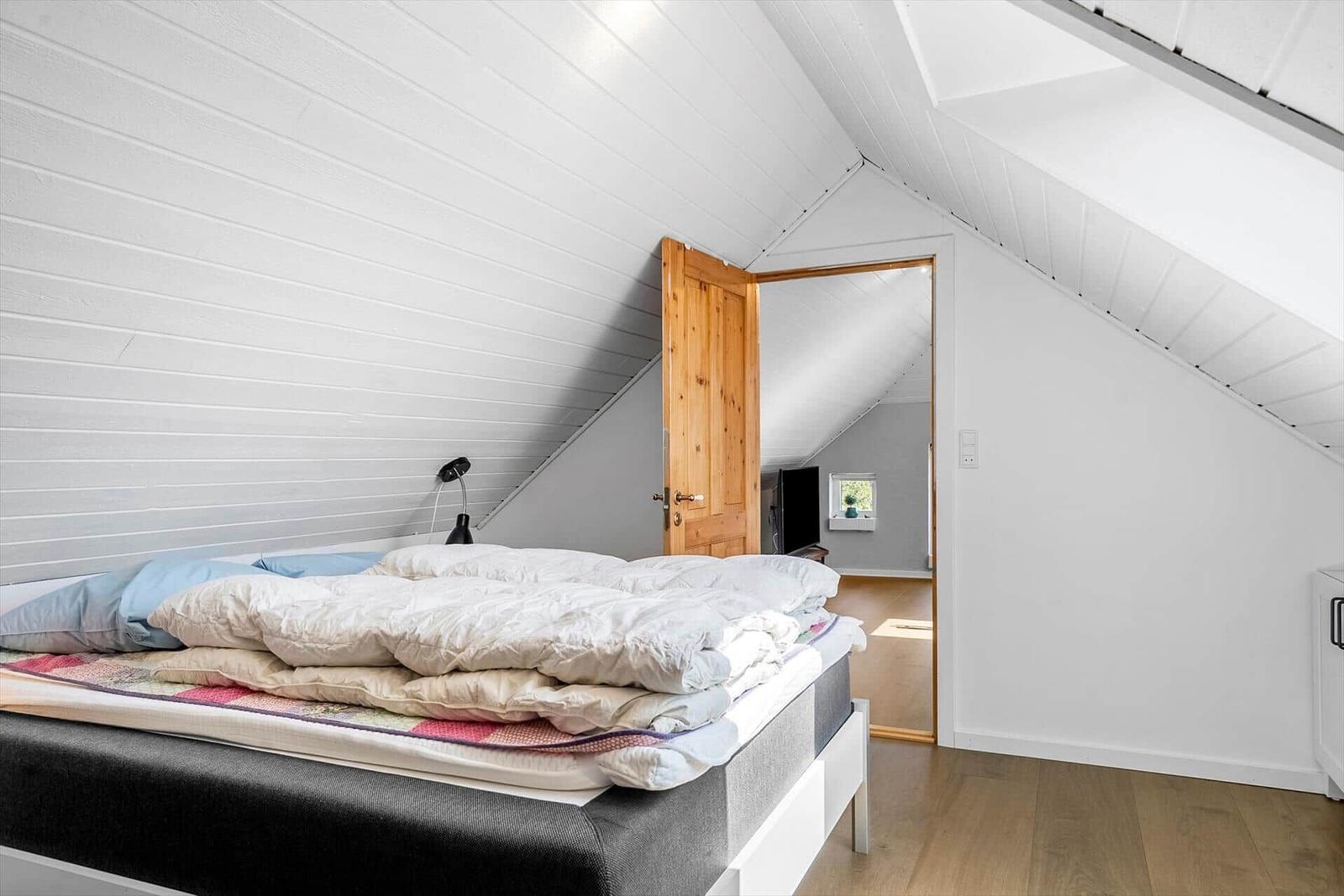 Schlafzimmer mit Dachschrägen, Bett und Tür zu einem weiteren Raum.