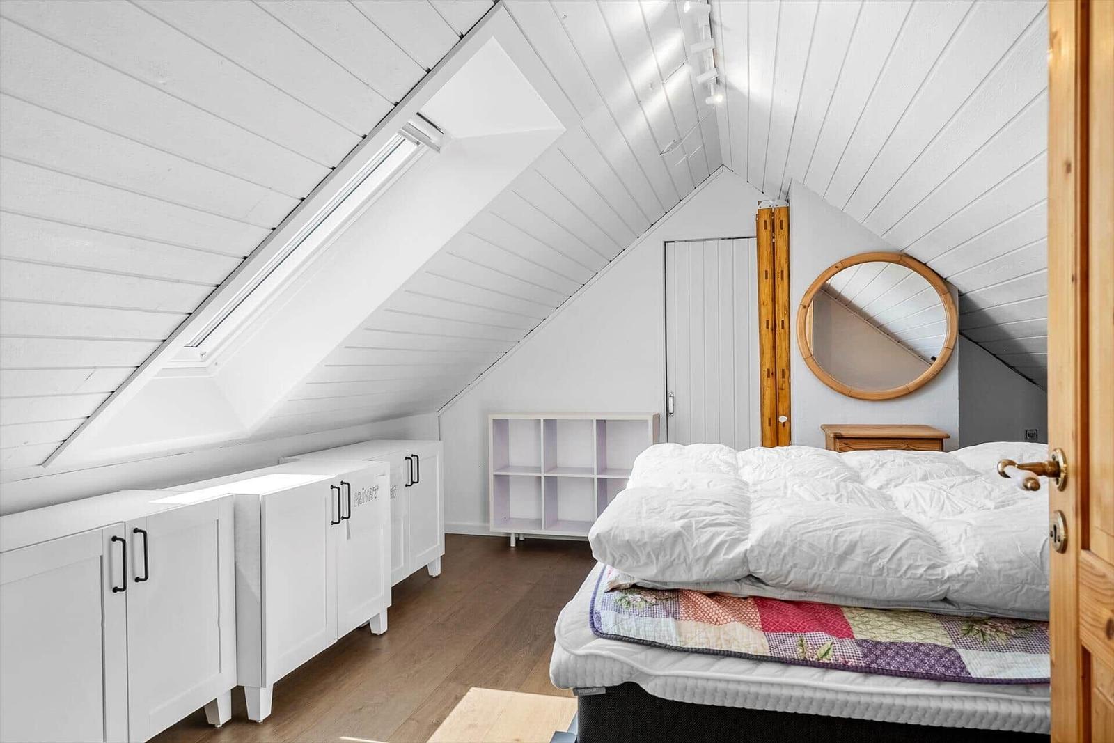 Schlafzimmer mit Dachschräge, Fenster, Bett und Schränken.
