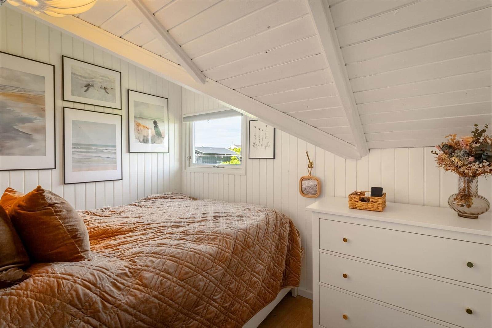 Schlafzimmer mit Bett, Schrank und Fenster unter Dachschrägen.
