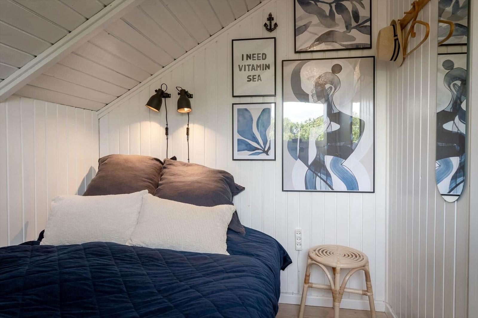 Schlafzimmer mit Bett, Wandbildern und Stehlampe.