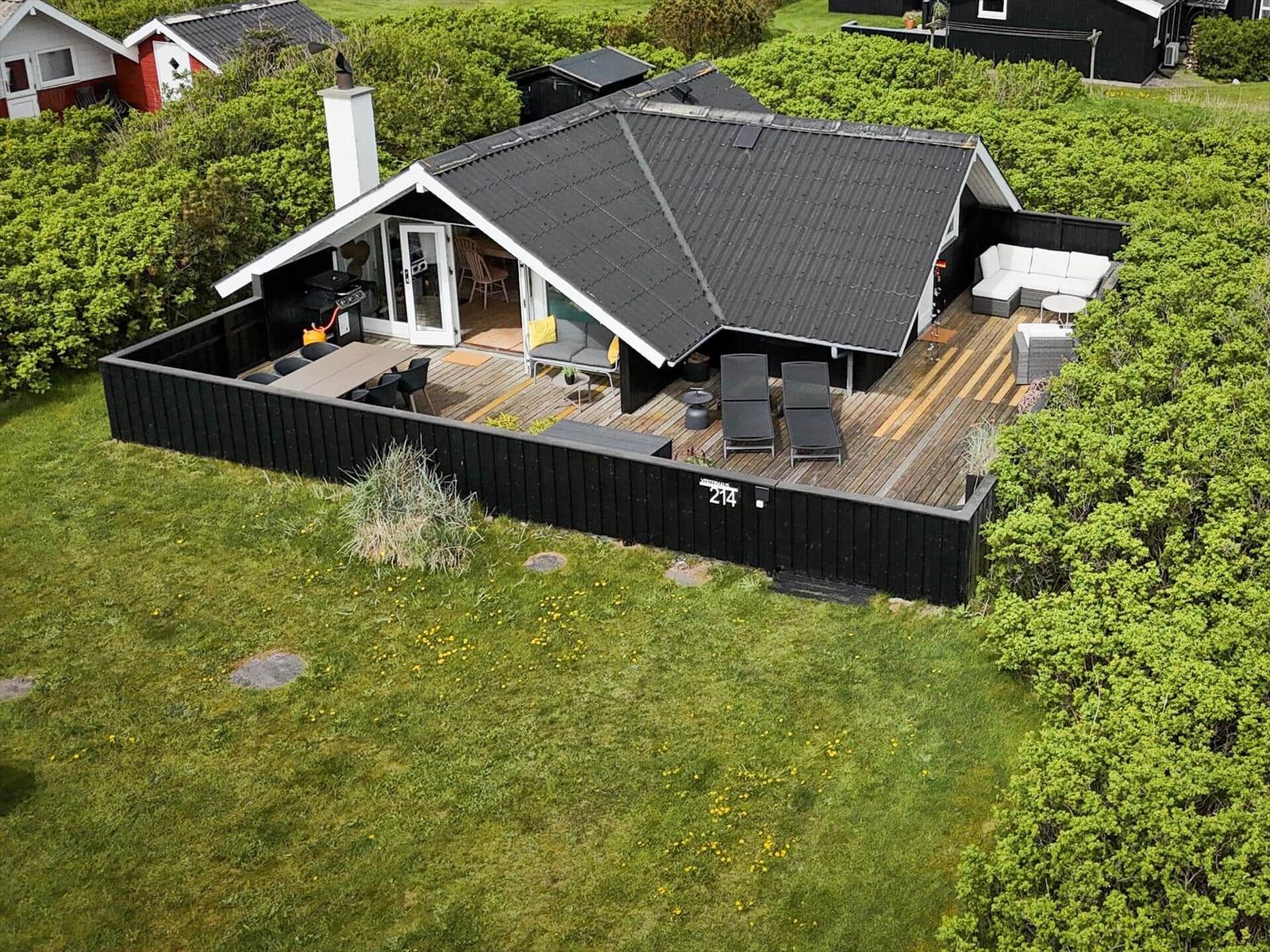 Modernes Haus mit großem Holzterrasse, Grill und Außensitzgelegenheiten.
