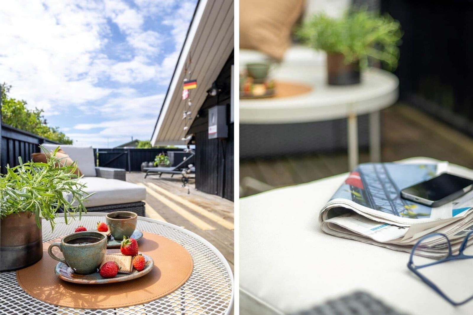 Terrasse mit Tisch, Kaffeetassen und Erdbeeren. Im Hintergrund liegt eine Liege.