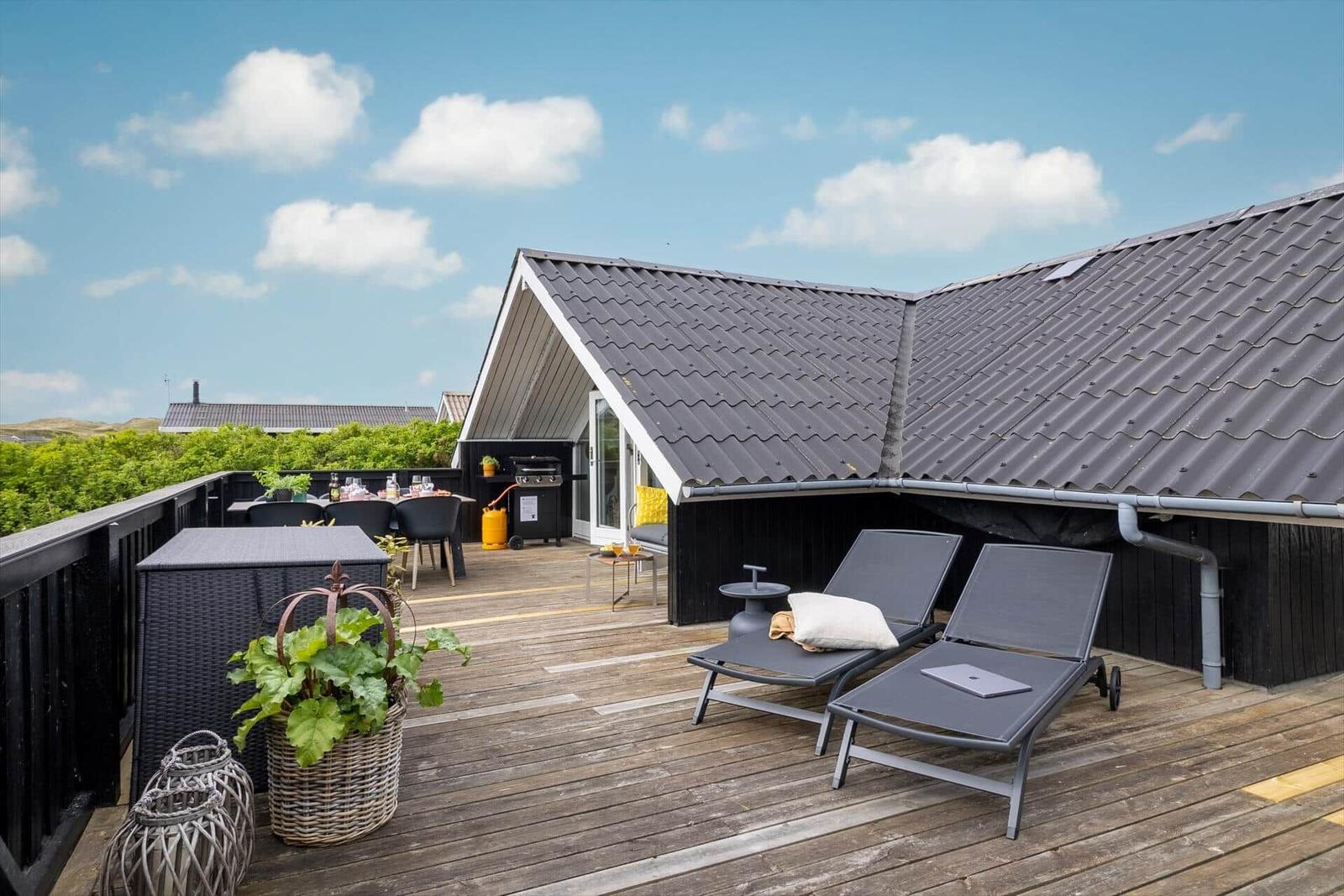 Terrasse mit Liegen, Grill und Tisch unter blauem Himmel.