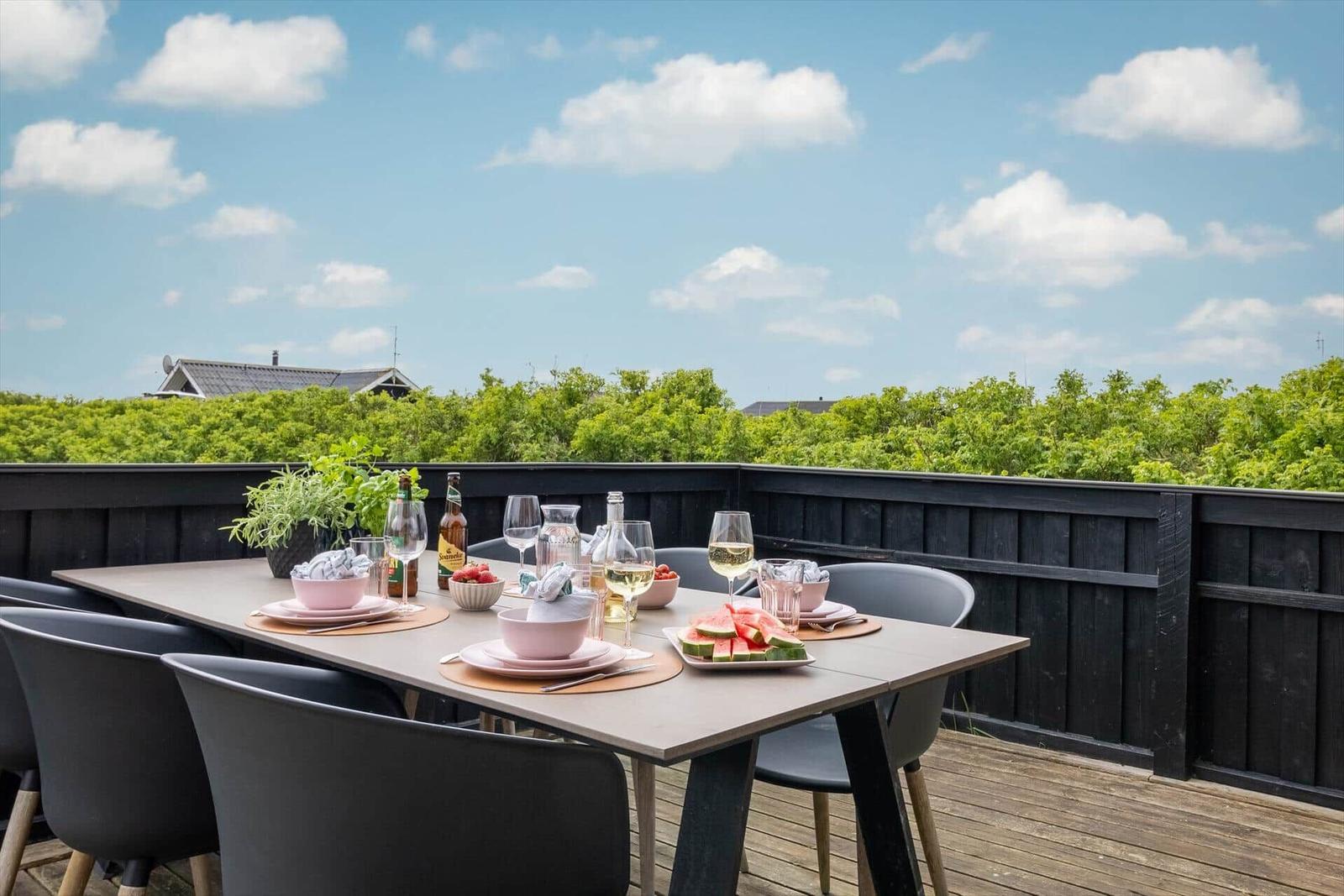 Terrasse mit Tisch und Stühlen, gedeckt mit Obst und Getränken, Blick auf grüne Vegetation.