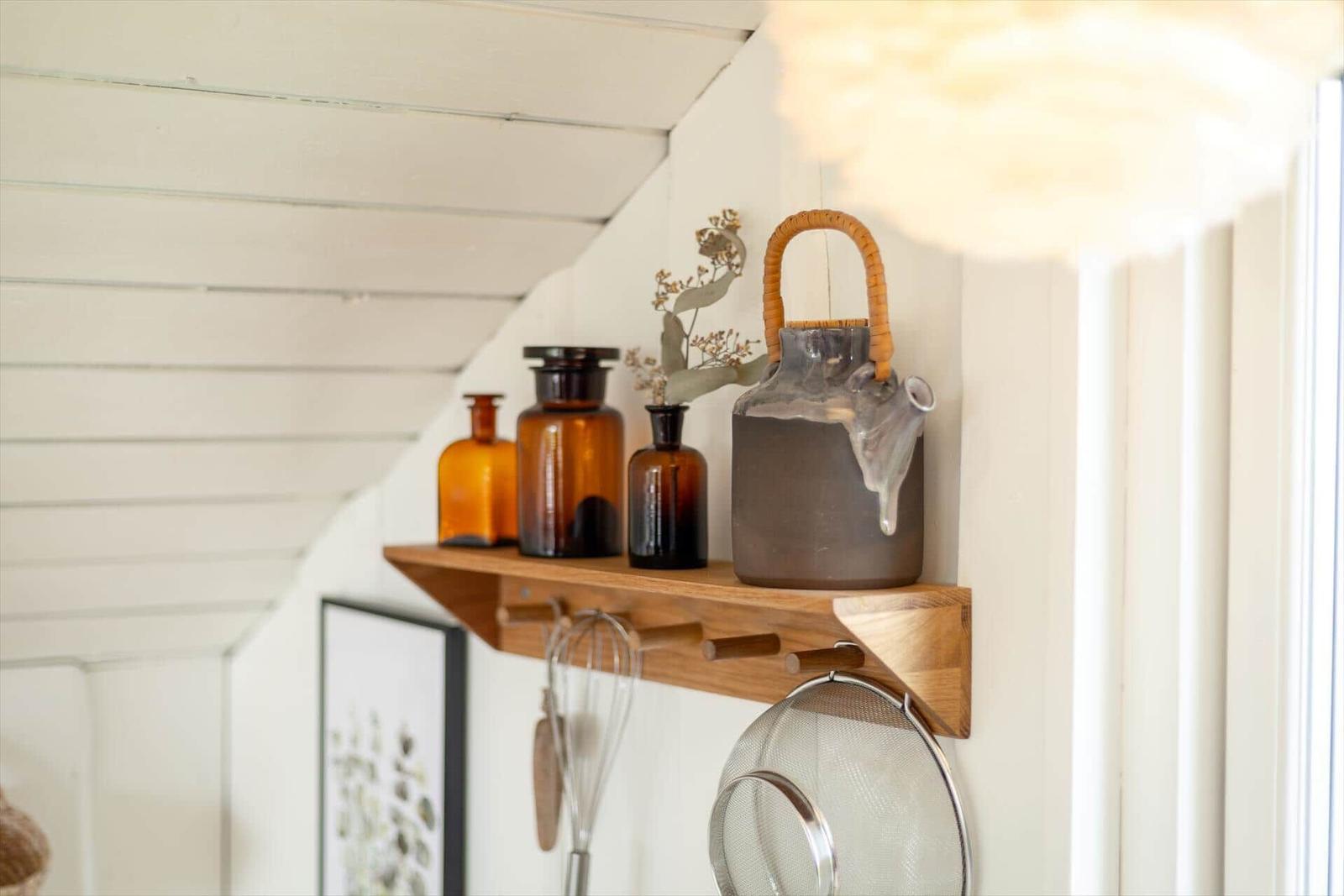 Holzregal mit Glasflaschen und Kanne an weißer Wand